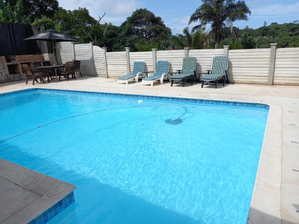 a large swimming pool with chairs and a table at Poolside Guest House in Port Shepstone