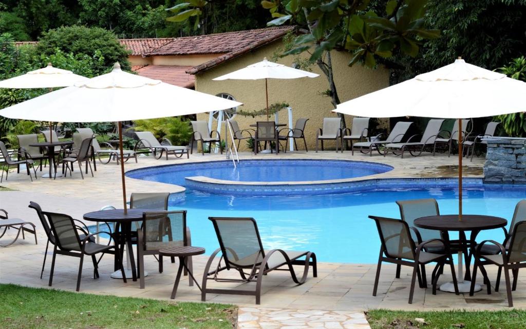 eine Gruppe von Tischen und Stühlen mit Sonnenschirmen neben einem Pool in der Unterkunft Hotel Santa Amalia in Vassouras
