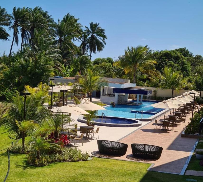 un complejo con piscina, sillas y palmeras en Flat Cantinho do Paraíso, en Guarajuba