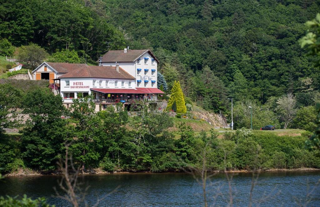 a large house on a hill next to a body of water at Logis Hôtel Belle Vue in Les Ancizes-Comps
