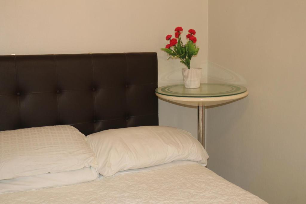 a bed with a table with a vase with red flowers on it at LUGAR DE DESCANSO in Ica