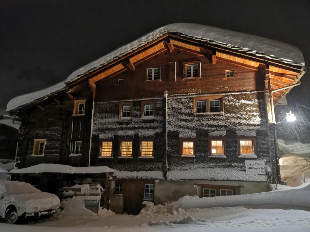 una casa de madera cubierta de nieve por la noche en B&B Gassa 95, en Vals