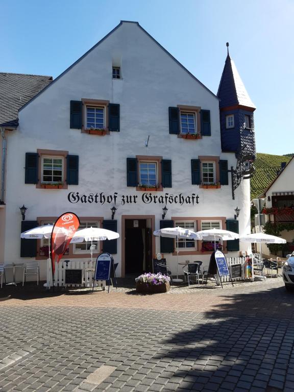 a white building with chairs and umbrellas in front of it at Gasthof Zur Grafschaft Veldenz in Veldenz