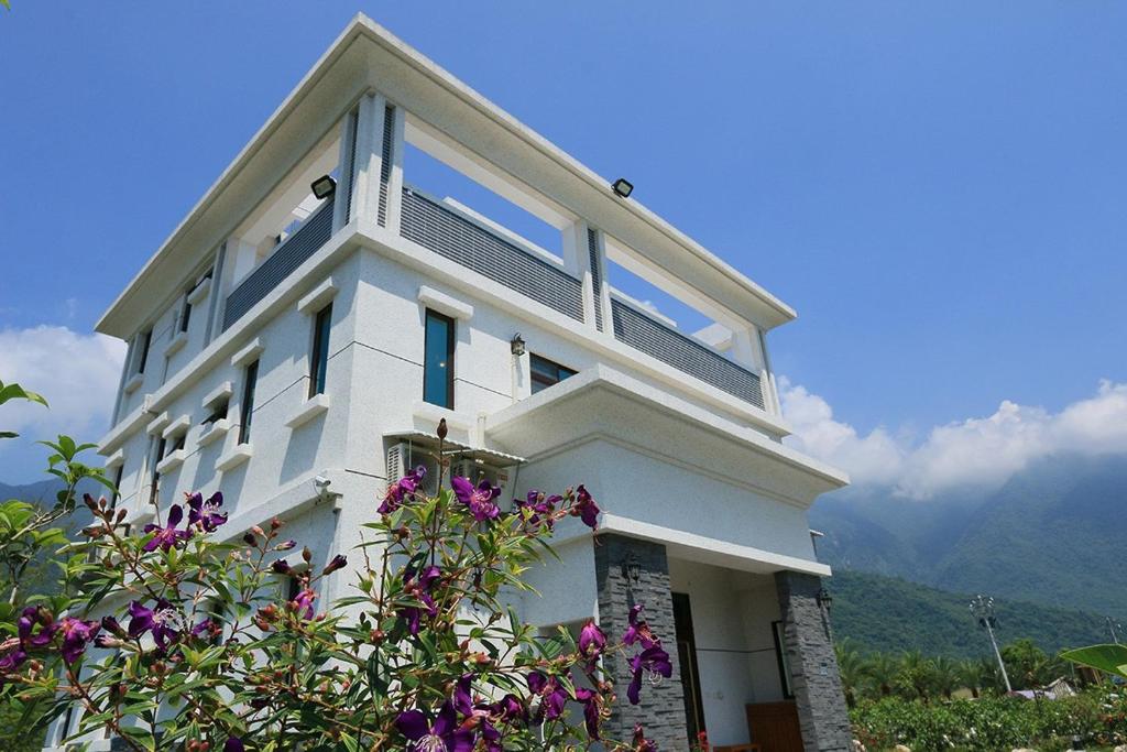 una casa bianca con fiori viola di fronte di Gully Orchard Homestay a Jialin
