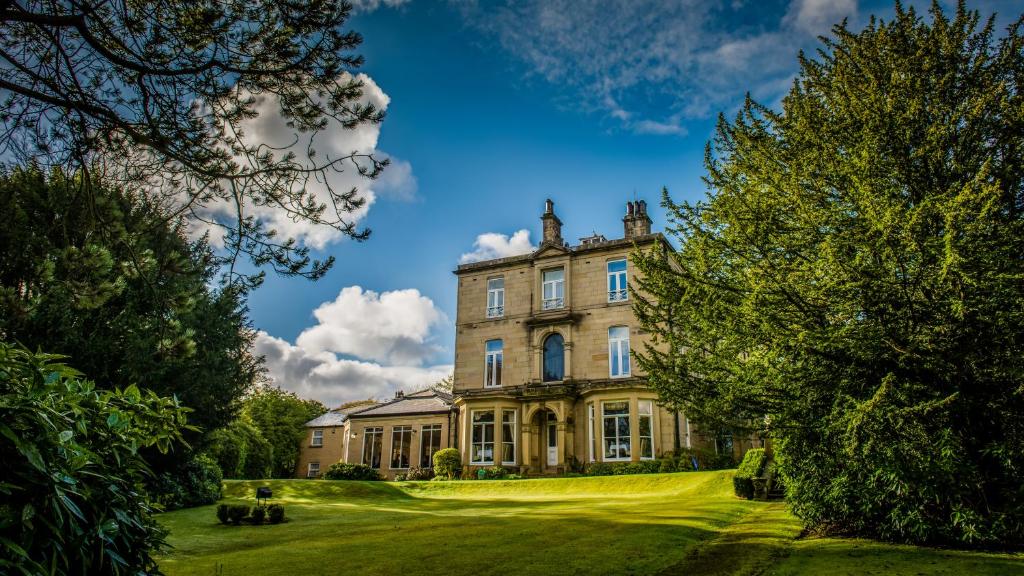 an old house on a green lawn with trees at Astley Bank Hotel in Darwen