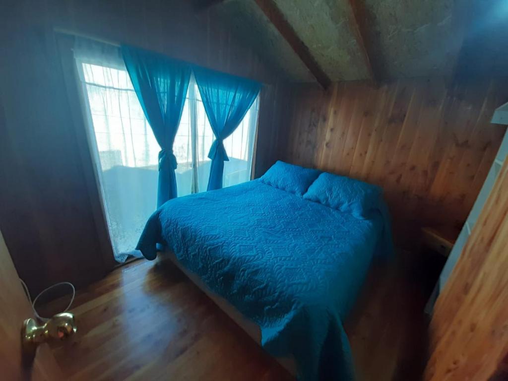 sypialnia z niebieskim łóżkiem i oknem w obiekcie Cabañas Costanera w mieście Villarrica