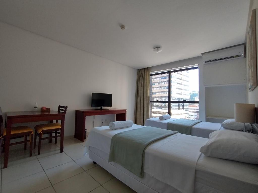 a hotel room with two beds and a desk and a window at Flat Athenas 611 in Salvador