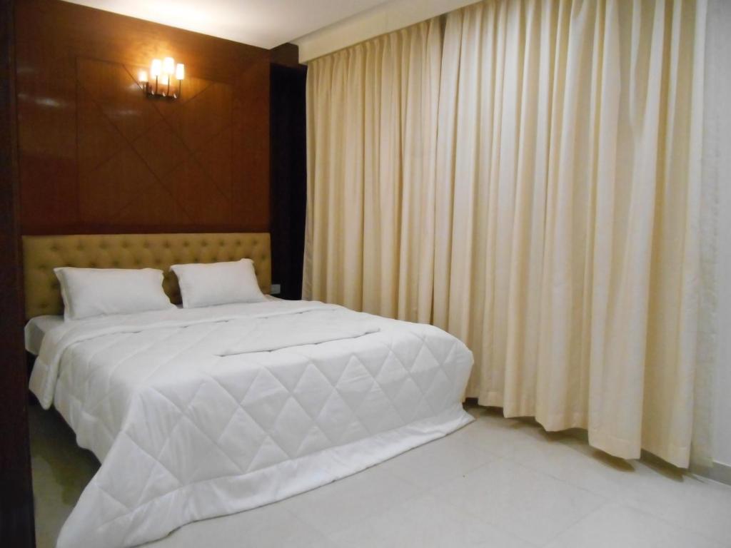 1 dormitorio con 1 cama blanca grande y cortinas en THE GRAND CORAL, en Bangalore