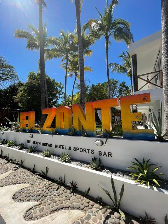 a sign for a hotel with palm trees in the background at The Beach Break Hotel El Zonte in El Zonte