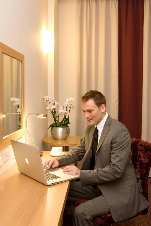 a man in a suit sitting at a desk with a laptop at Leonardo Hotel Aberdeen in Aberdeen