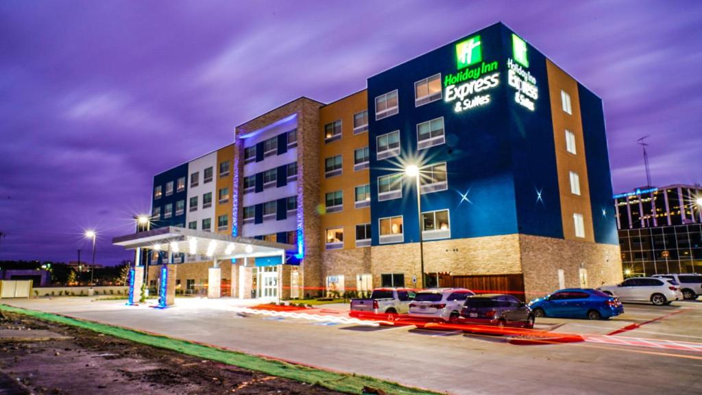 Holiday Inn Express & Suites - Dallas Market Center, an IHG Hotel في دالاس: فندق فيه سيارات متوقفة في مواقف