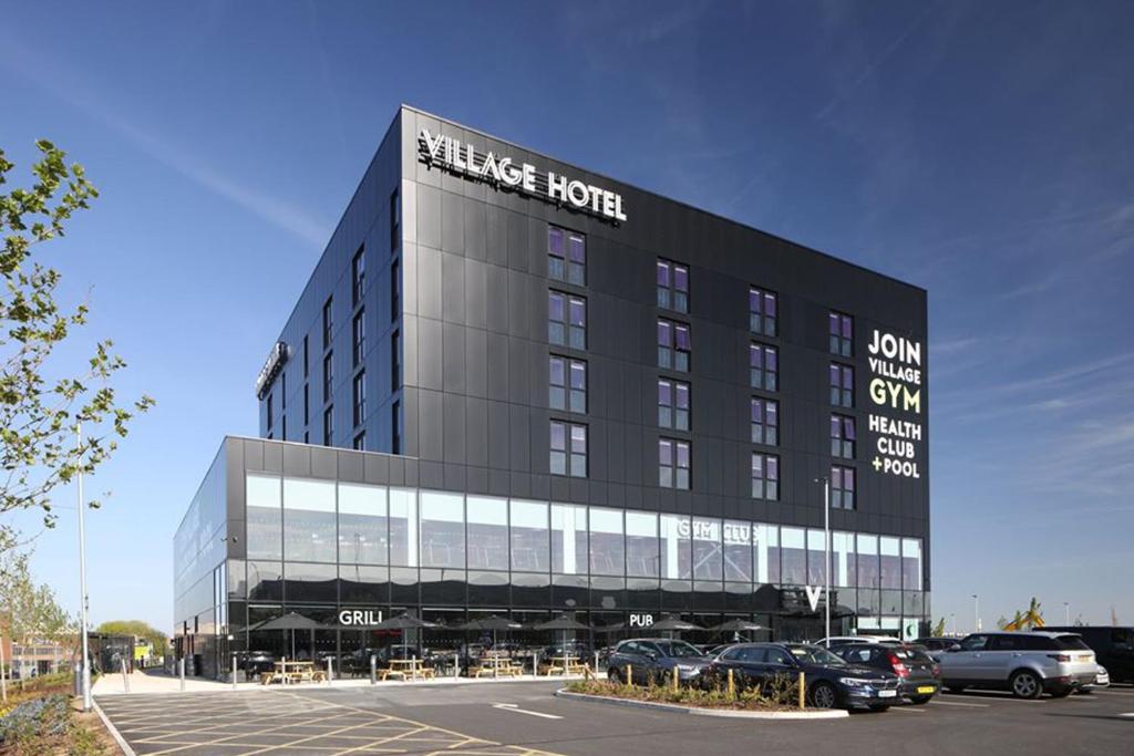 Village Hotel Southampton Eastleigh في ساوثهامبتون: مبنى كبير به سيارات تقف في موقف للسيارات