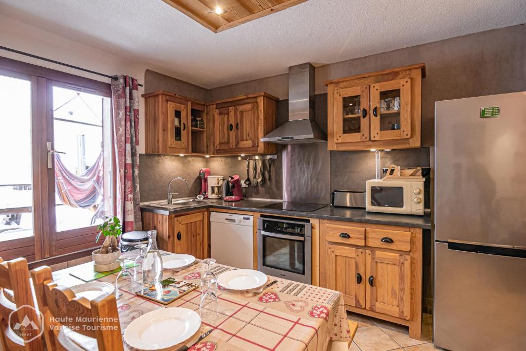 a kitchen with wooden cabinets and a table and a refrigerator at La Soldanelle in Lanslevillard