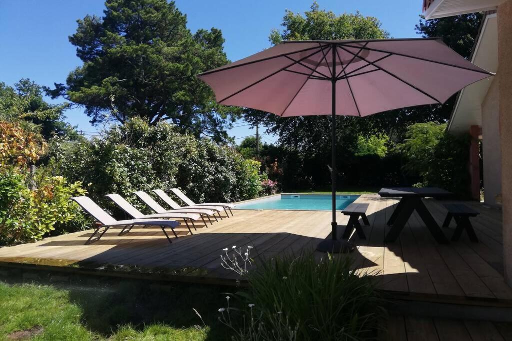 - une terrasse avec une table et un parasol à côté de la piscine dans l'établissement Grande maison familiale piscine et jardin, à Gujan-Mestras