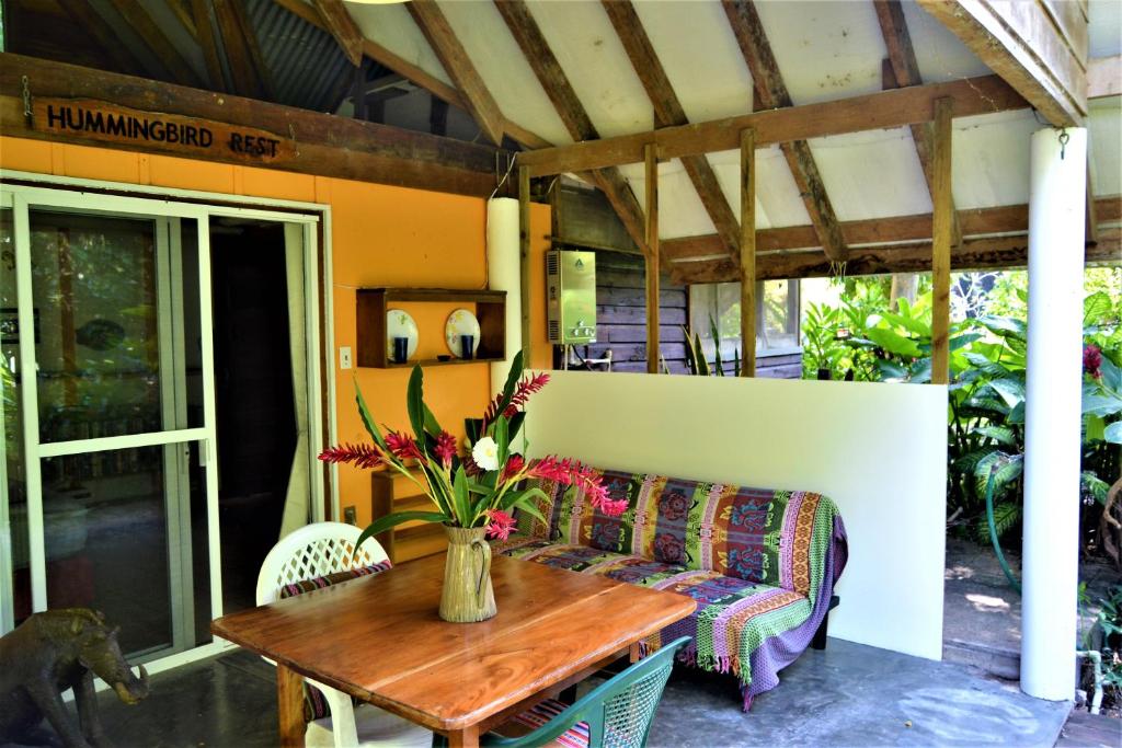 een bank en een tafel met bloemen op een patio bij Hummingbird Rest a fully equipped cabana in subtropic garden in San Ignacio