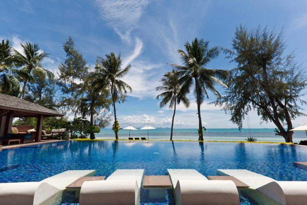a pool with chairs and the ocean in the background at Baan Kilee in Lipa Noi