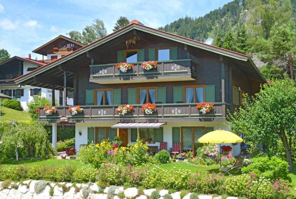 ein Haus mit Blumen auf den Balkonen und einem Sonnenschirm in der Unterkunft Gästehaus Sonnenhang in Reit im Winkl