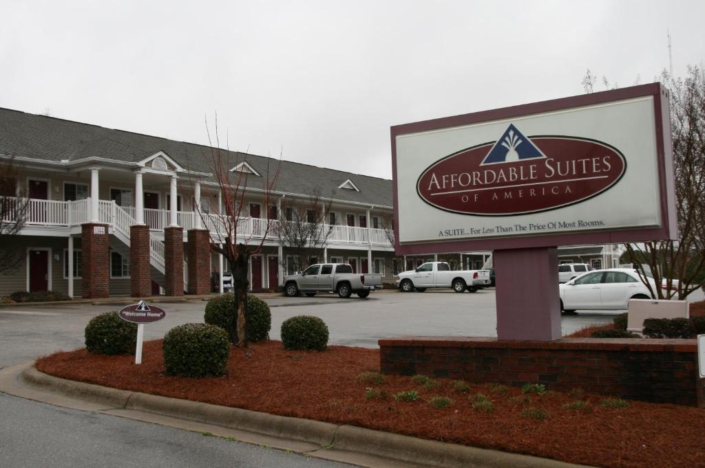 um sinal em frente a um edifício com carros num parque de estacionamento em Affordable Suites Rocky Mount em Rocky Mount