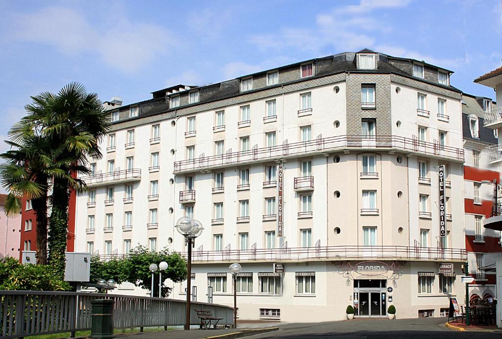a large white building with a palm tree in front of it at Hôtel Florida in Lourdes