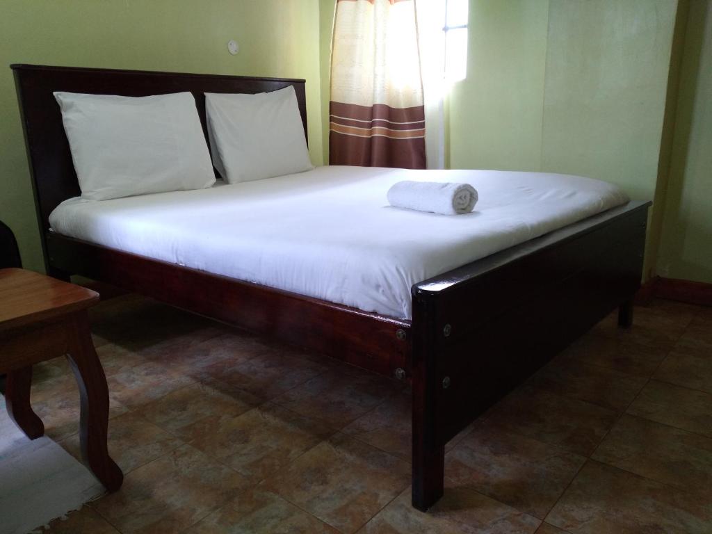 a bed with a wooden frame and white sheets at Crown Hotel Kericho in Kericho
