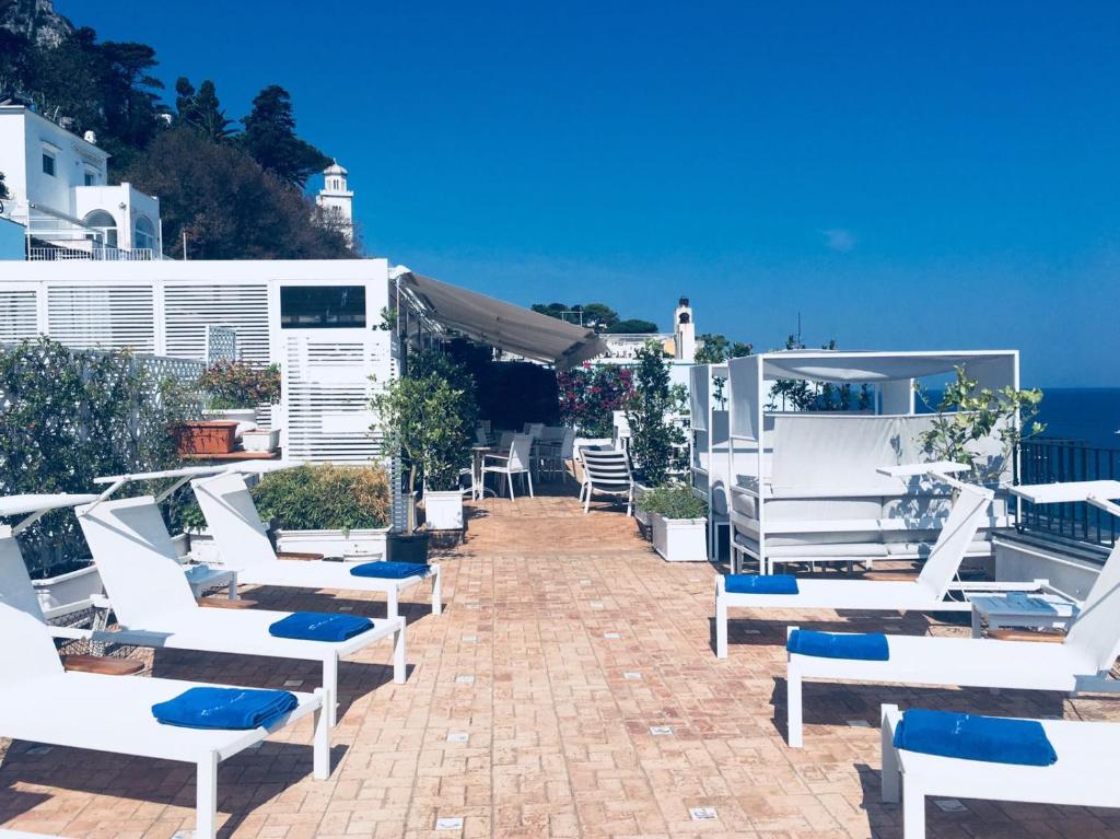 a patio with white chairs and the ocean in the background at Relais Maresca Luxury Small Hotel & Terrace Restaurant in Capri