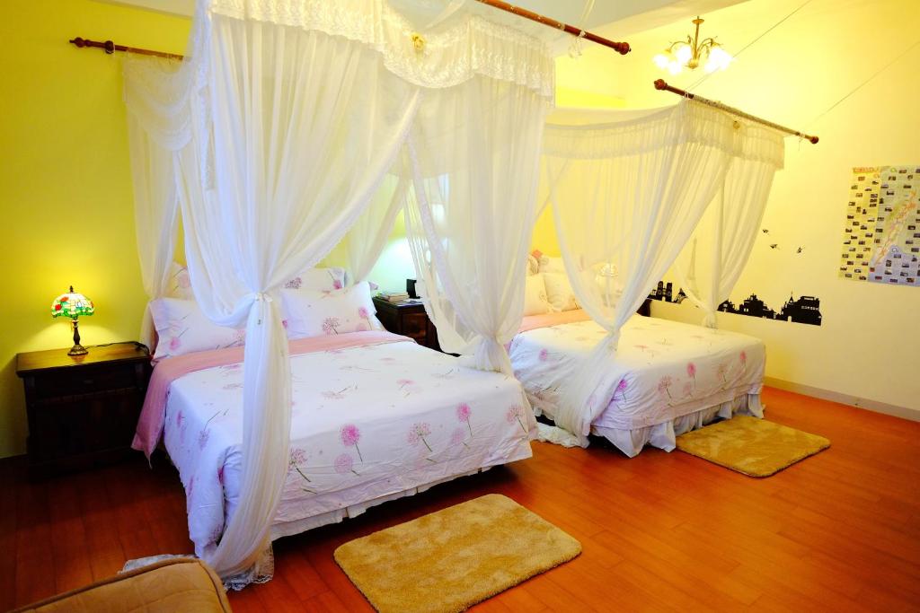 two beds in a bedroom with white curtains and wood floors at Spring Garden Homestay in Hualien City