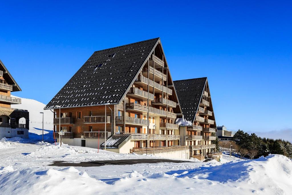 um grande edifício de madeira na neve com neve em O - Sancy Résidence de Tourisme em Super Besse