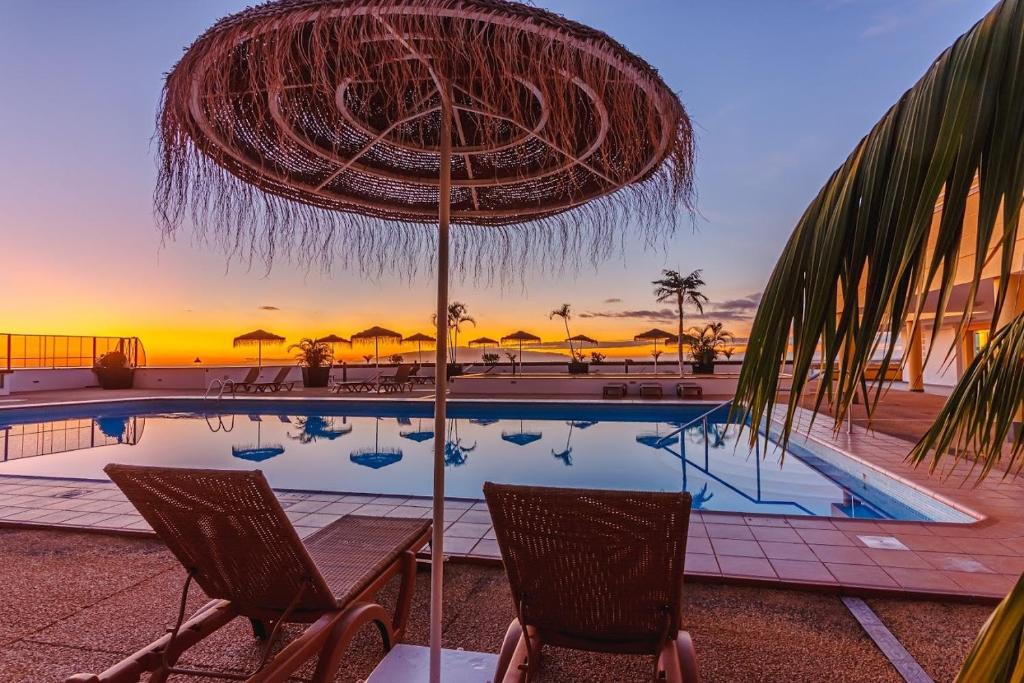 een parasol en stoelen naast een zwembad bij Vista Impresionante SunSet Breathtaking view WiFi in Adeje