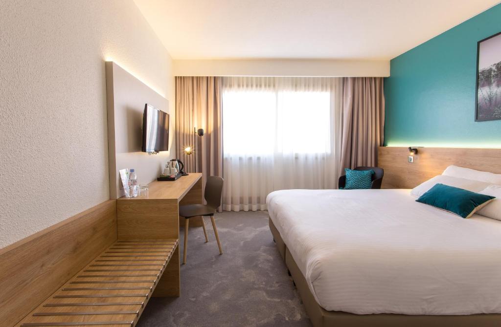 ヴィルールバンヌにあるホテル デ コングレのベッドとデスクが備わるホテルルームです。