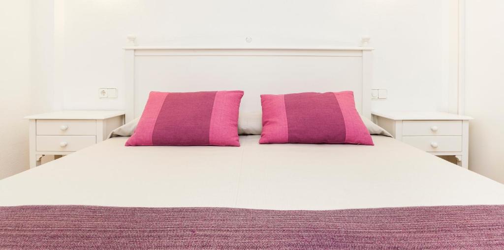a white bed with two pink pillows on it at Insotel Club Tarida Playa in Cala Tarida