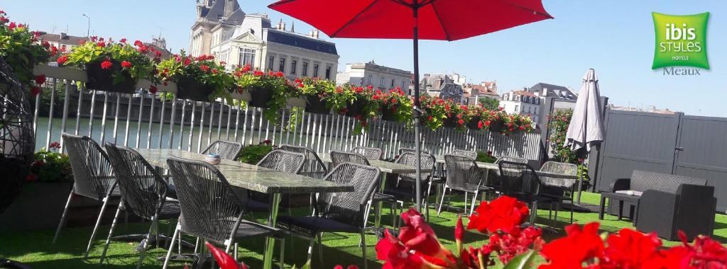 una mesa con sillas, una sombrilla y flores en una valla en ibis Styles Meaux Centre, en Meaux