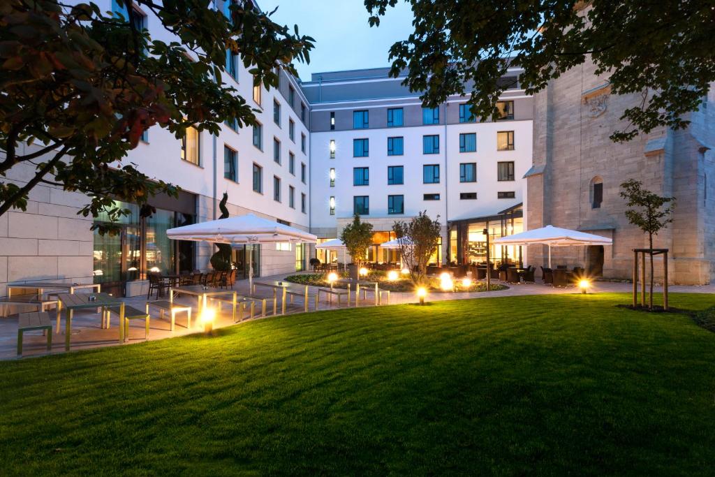 a lawn in front of a building with tables and umbrellas at Steigenberger Parkhotel Braunschweig in Braunschweig