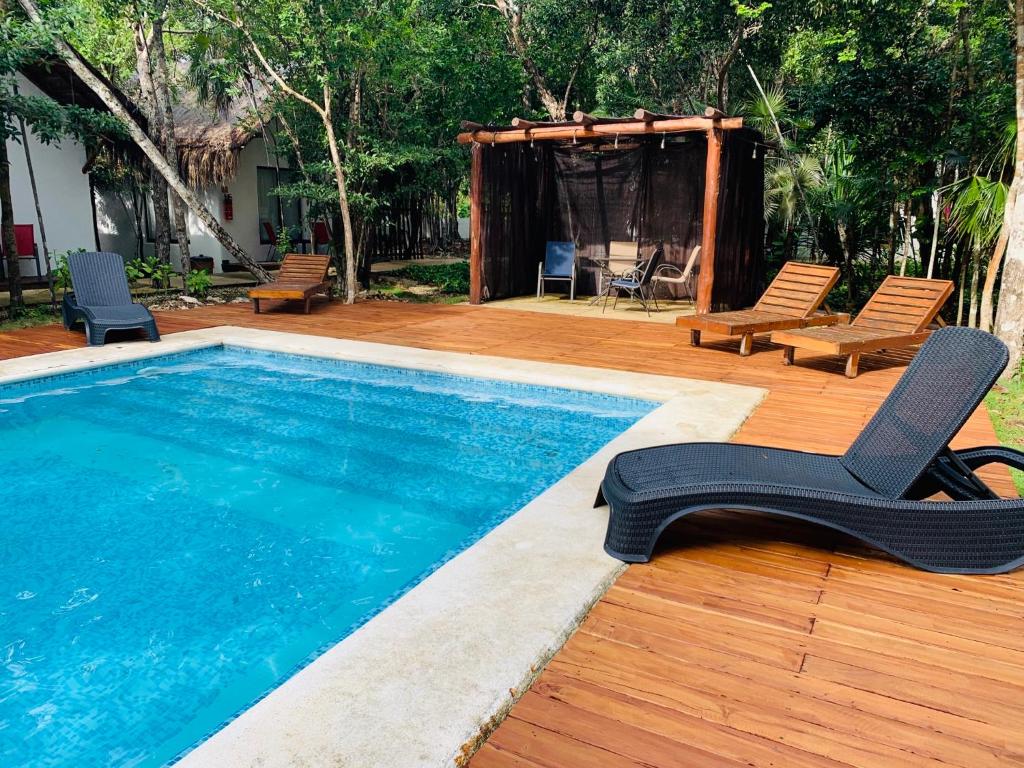 a swimming pool with two chairs and a wooden deck at Ecovergel Hotel Riviera Maya in Chemuyil