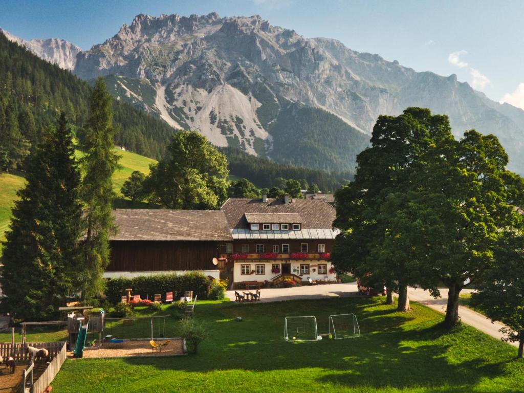 un bâtiment en face d'une montagne avec un champ et des arbres dans l'établissement Zeiserhof, à Ramsau am Dachstein