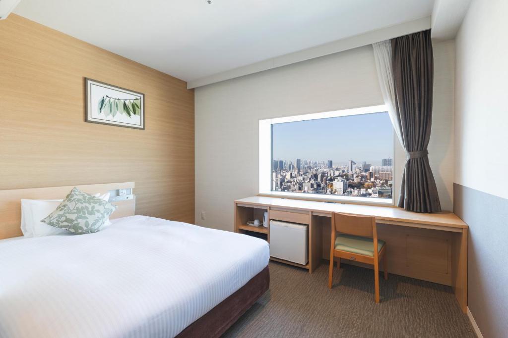 a hotel room with a bed and a desk and a window at Hotel Crown Hills Ueno Premier in Tokyo