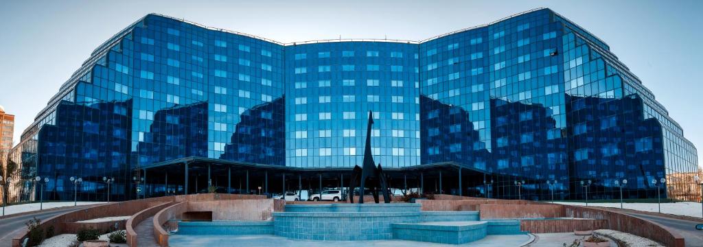 a large glass building with a fountain in front of it at River Palace Hotel in Atyraū