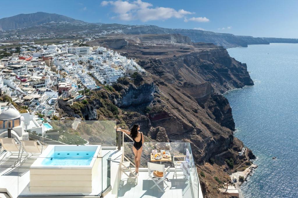 una donna sul bordo di un balcone con vista sull'oceano di Mythical Blue Luxury Suites a Firà