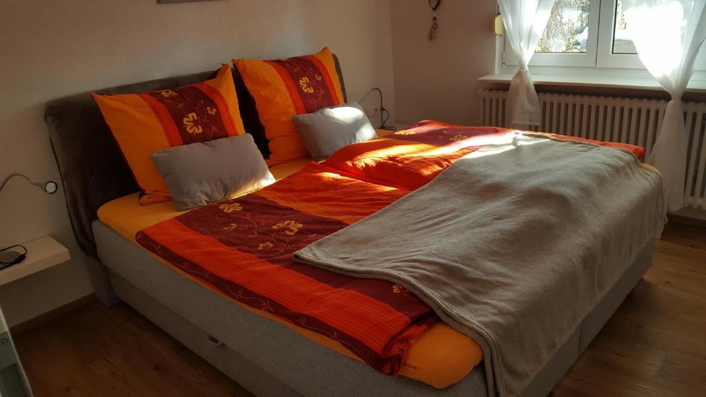 een bed met een oranje deken en kussens erop bij Ferienwohnung Miezerle in Steißlingen