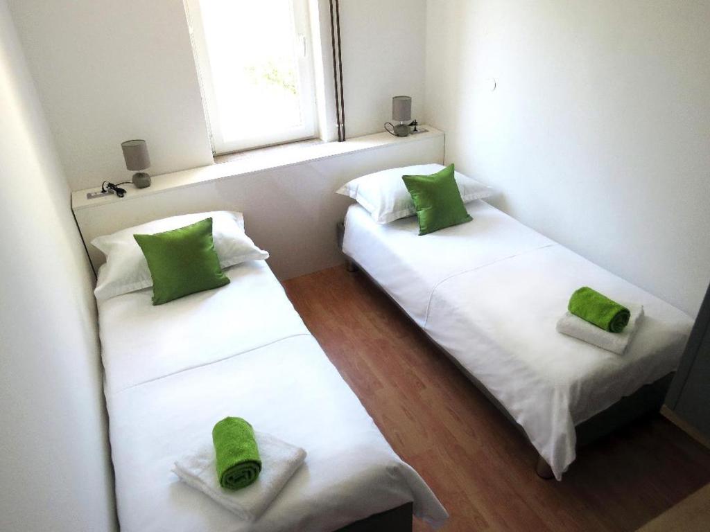 2 łóżka w pokoju z zielonymi poduszkami w obiekcie Apartmani Alta w Krku