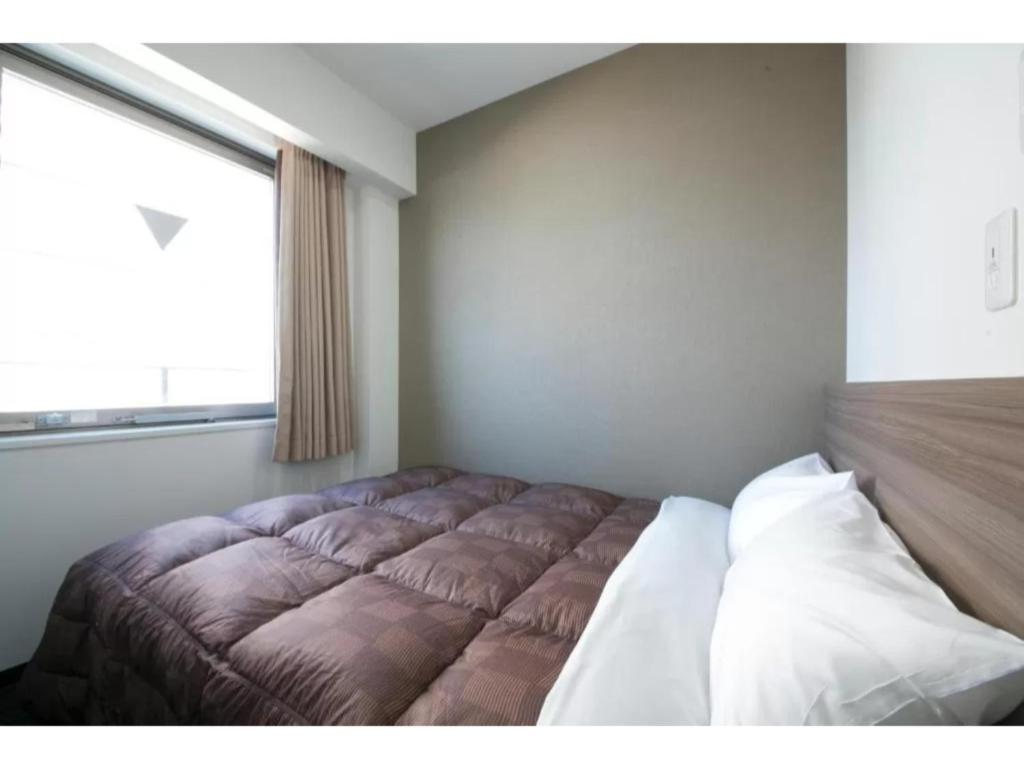 uma cama num quarto com uma grande janela em R&B Hotel Shin Osaka Kitaguchi - Vacation STAY 15208v em Osaka