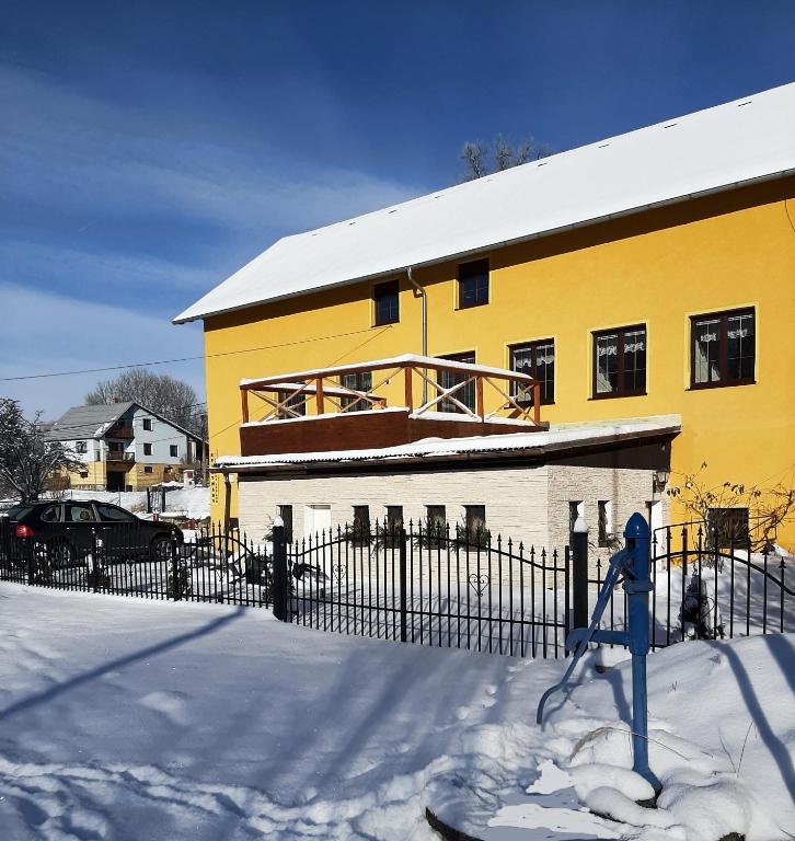 żółty dom z płotem w śniegu w obiekcie Apartmány-Zámecká restaurace w mieście Jindřichovice