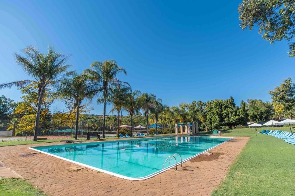 a swimming pool in a park with palm trees at Sparkling Water Hotels & Spa in Rustenburg