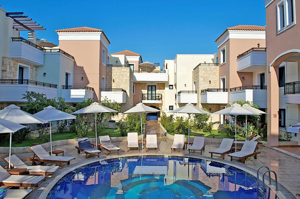 a swimming pool with chairs and umbrellas next to buildings at Caldera Bay in Plataniás