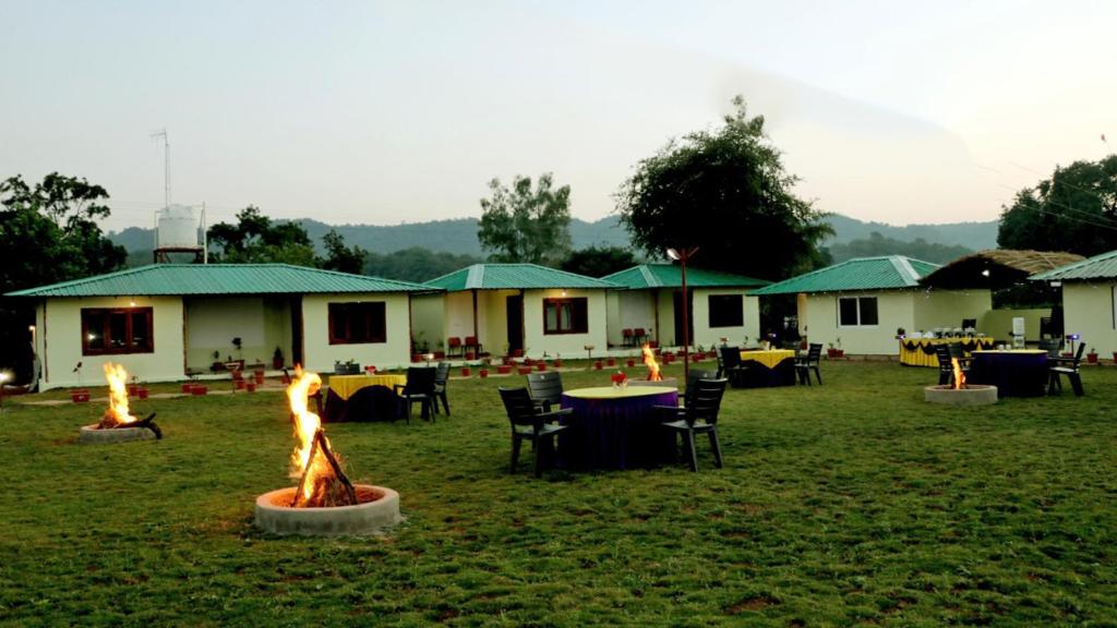 a group of lodges with tables and fires in the grass at Moustache Panarpani Retreat in Pachmarhī