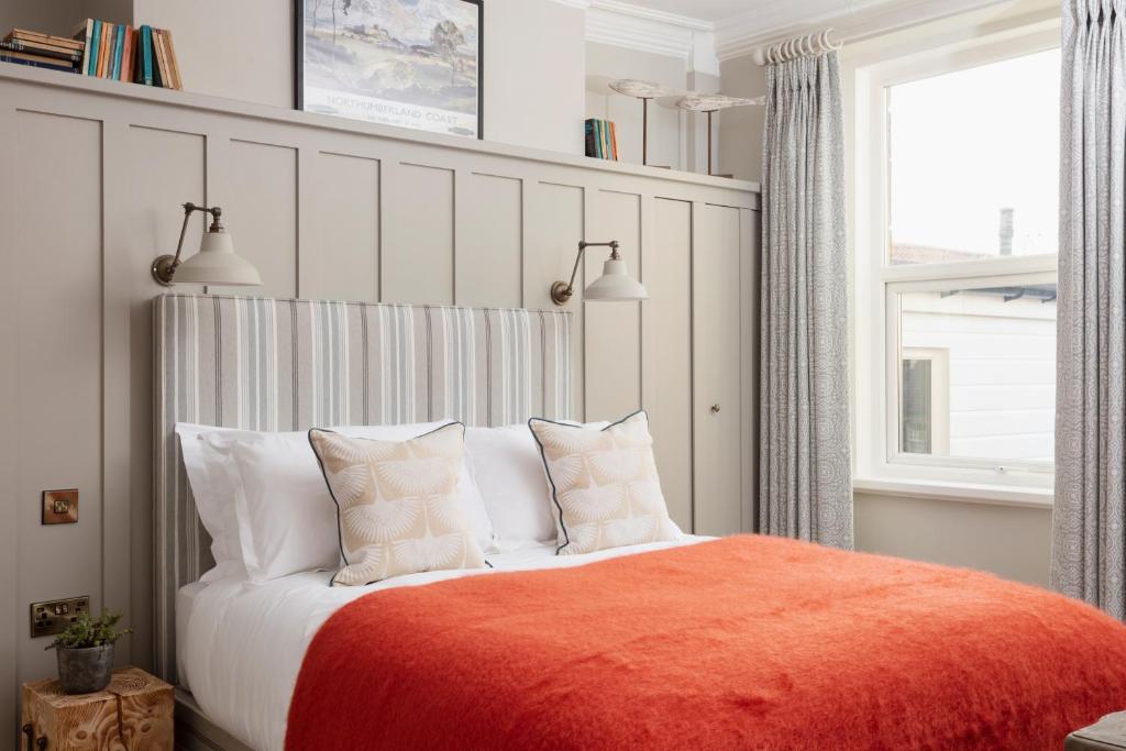 a bedroom with a bed with an orange blanket and pillows at The Whittling House in Alnmouth