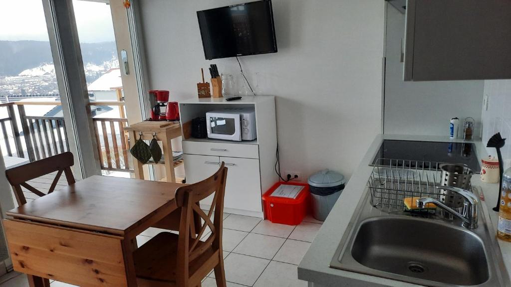 eine Küche mit einem Tisch, einer Spüle und einer Mikrowelle in der Unterkunft F2 SUR LES HAUTEURS DE GERARDMER in Gérardmer