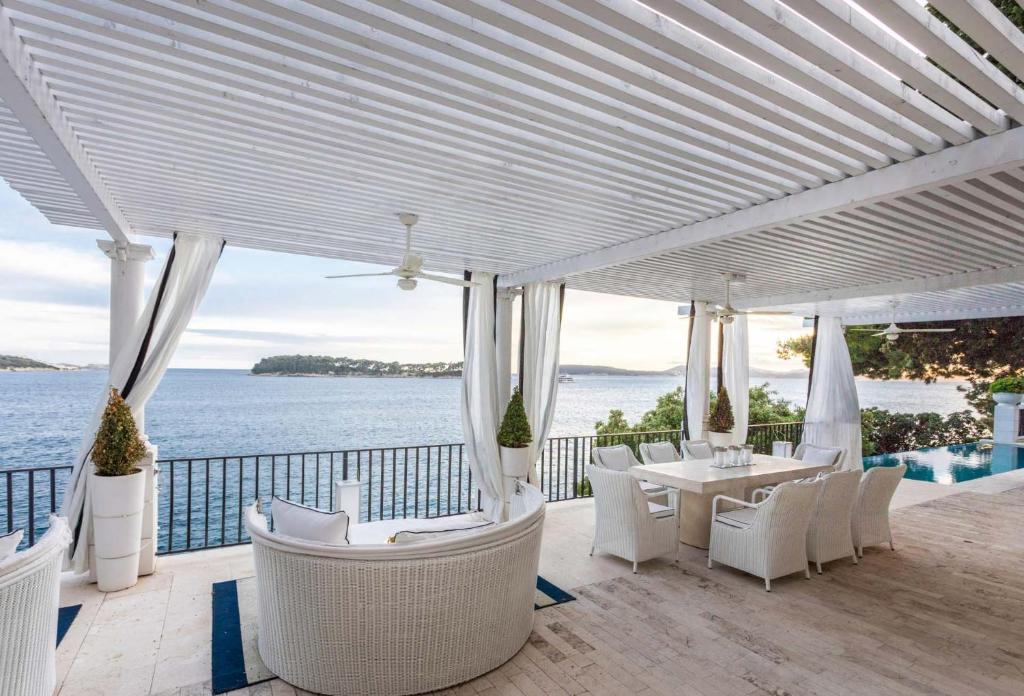 Villa Dubrovnik Palazio A Stunning 4 Bedroom Villa On the Waters Edge في دوبروفنيك: فناء مع كراسي بيضاء وطاولات والمحيط