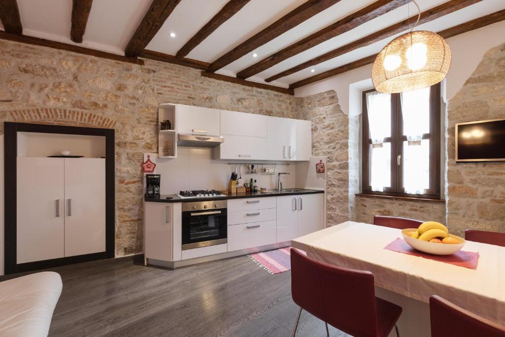 a kitchen with white cabinets and a table with a bowl of fruit at Apartman Arca in Rovinj