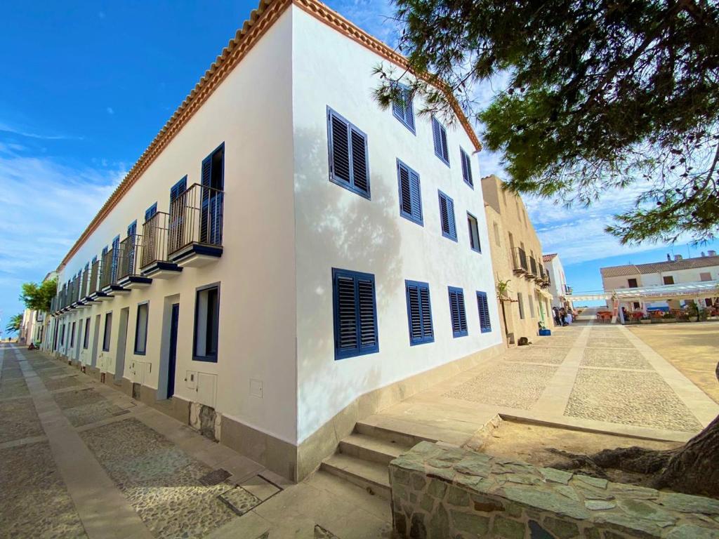 ein weißes Gebäude mit blauen Rollläden auf einer Straße in der Unterkunft Apartamentos Vientos de Tabarca in Tabarca