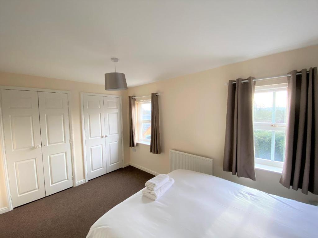 a bedroom with a white bed and two windows at Johnson Townhouse in Wellingborough